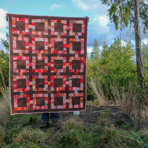 Quilt pattern in a mid-century modern theme in red and brown with blue sky behind