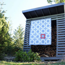 Load image into Gallery viewer, Shinersview connected squares quilt pattern hanging in gray and white with a red square hanging on a woodshed outdoors