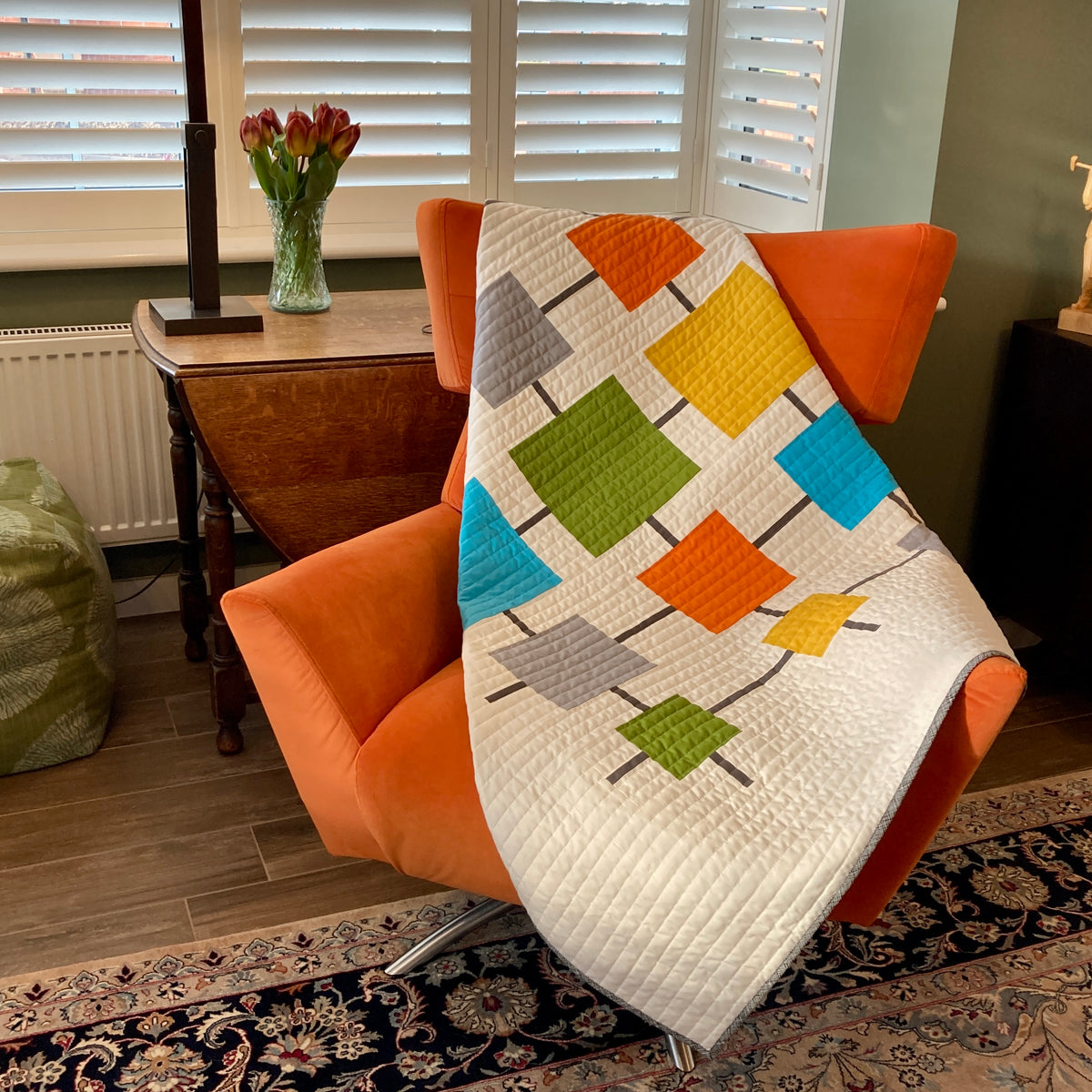 White quilt with brightly colored squares on an orange mid-century modern chair