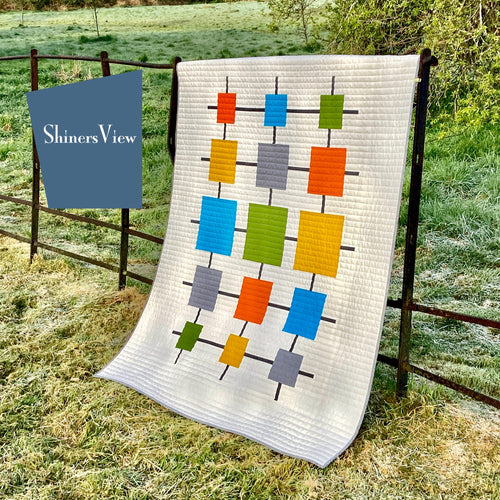White quilt with colored squares hanging on old fence in green field